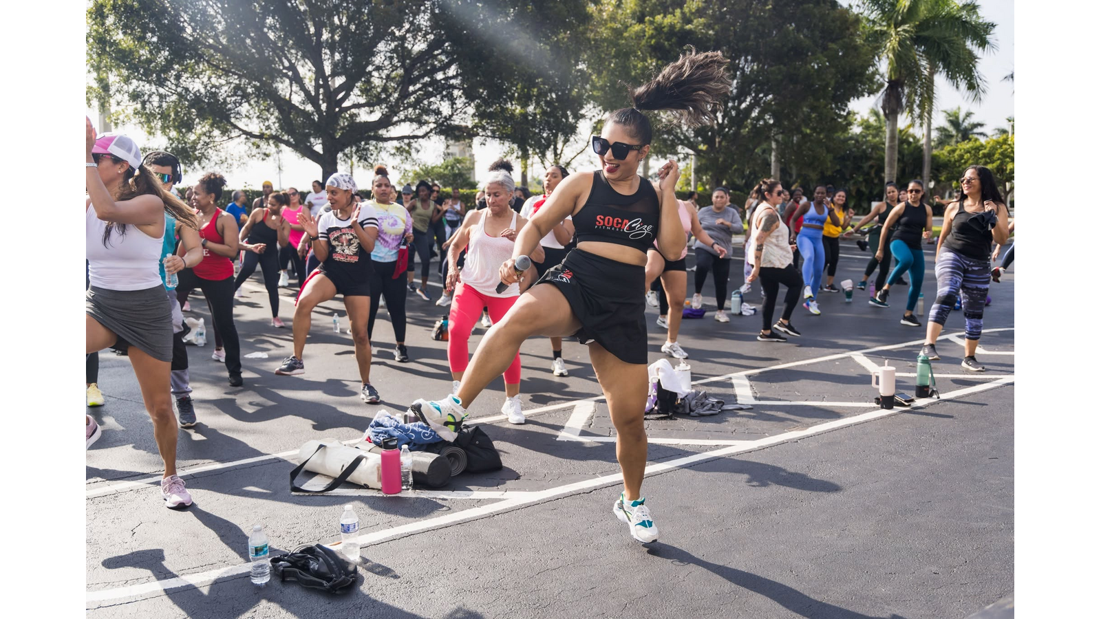 Group of people doing outdoor dance fitness class in a parking lot with palm trees